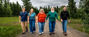 A group walks together on a winding dirt trail through lush green forest on an overcast day.