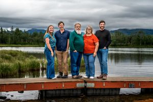 Family group posing on a wooden dock by a scenic lake with mountains in the distance.