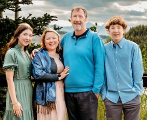 Four people pose together outdoors against a mountainous backdrop with evergreen trees.