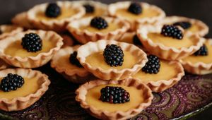 Mini lemon tarts topped with fresh blackberries on a decorative plate.