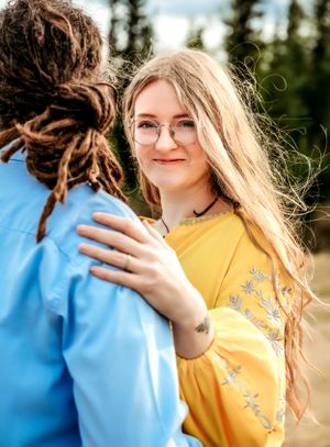 Person in yellow embroidered dress with person in blue jacket outdoors.