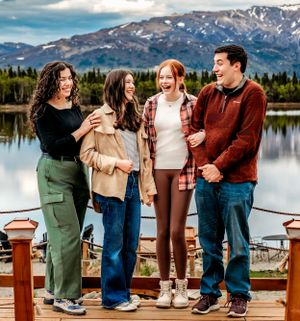 Friends laughing together on lakeside deck with mountain backdrop.