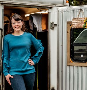 Person wearing teal sweater stands in doorway of white trailer.