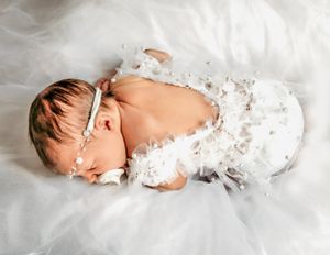 Newborn baby sleeps peacefully wrapped in white lace on soft fabric.