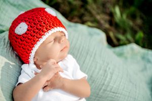 Baby wearing red and white crochet hat rests on mint green blanket.