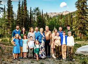 Large extended family group poses together on mountain trail with peaks and forest behind them.