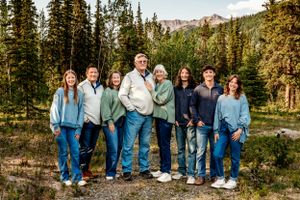 A large group stands together for a portrait with mountains and forest scenery in the background.