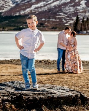 A child stands confidently on a rock with a scenic mountain lake backdrop.