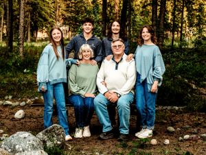 A multi-generational group poses for a portrait in a wooded forest setting with rocks and trees.