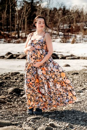A flowing floral maternity dress catches the wind against a snowy winter landscape.