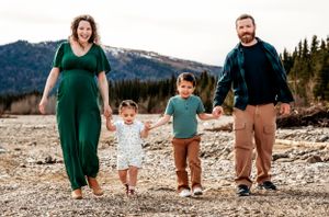 Family walking together on rocky beach with mountain backdrop.