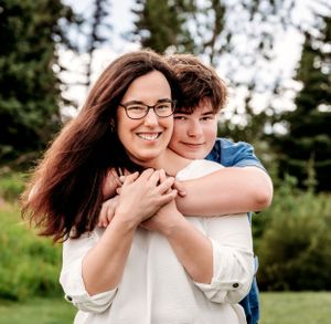 A joyful piggyback embrace captured outdoors with evergreen trees in the background.