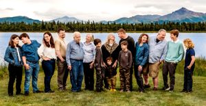 A large extended family group poses together by a lake with mountains visible in the distance.