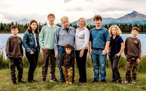 A multi-generational group poses by a scenic lake with mountains and evergreen trees in the background.