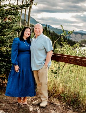 A couple poses together on a mountain trail with dramatic cloudy skies and forest views.