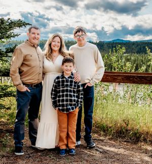 A family of four poses together on a mountain overlook with dramatic clouds in the background.