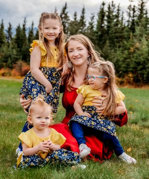 A family portrait set in front of evergreen trees with matching floral dresses and yellow accents.