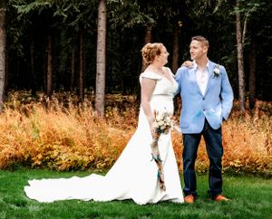 A wedding couple poses together on grass with golden ferns and forest trees in the background.