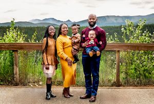 Family stands together on wooden deck overlooking mountain vista in autumn setting.