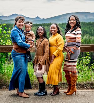 A family wearing coordinated brown and yellow outfits poses together in a scenic mountain meadow setting.