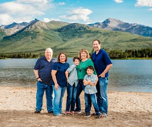 A group stands together on a beach with mountains and a lake in the background on a sunny day.