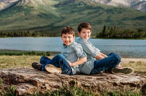 Two children lying on a rocky outcrop with mountains and a lake in the scenic background.