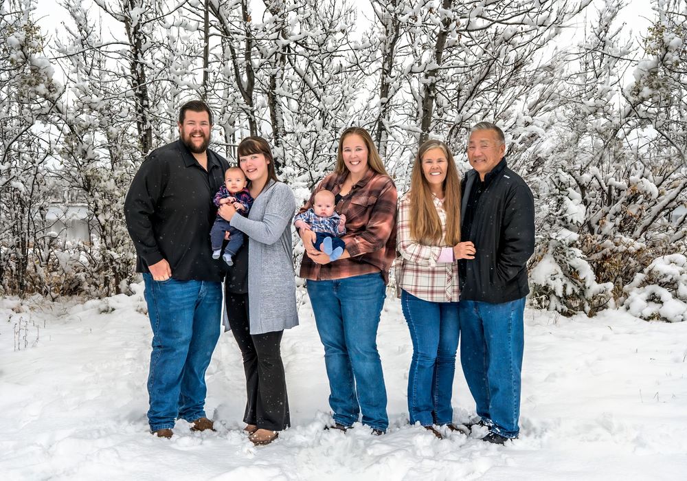 A family group poses together in a snowy winter landscape wearing coordinating blue and neutral colored outfits.