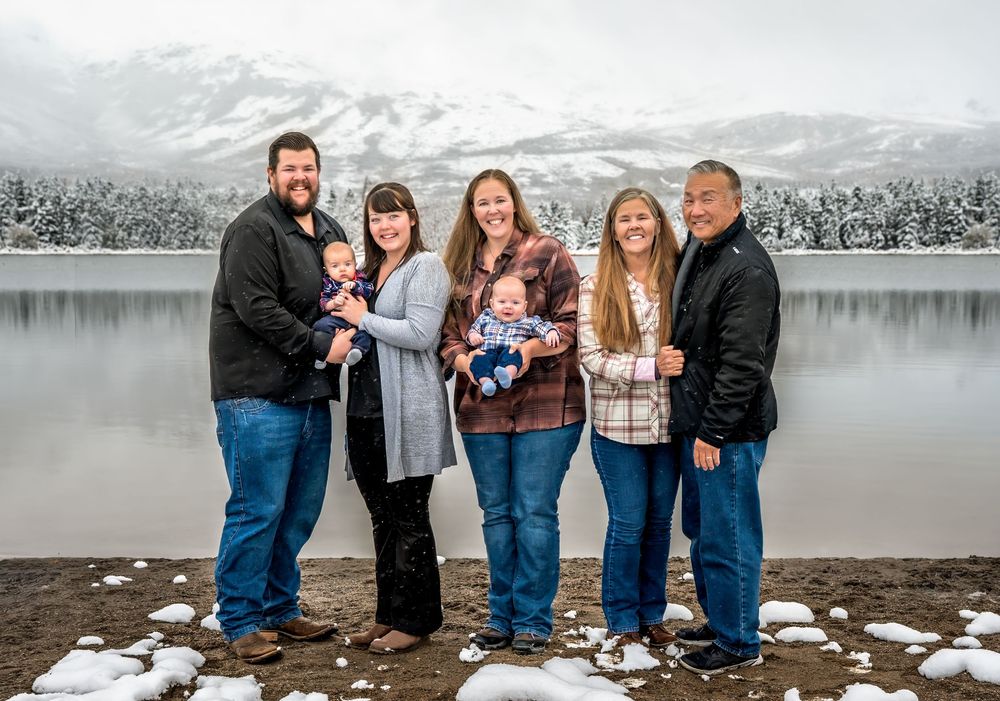 Family group poses together in winter scene by snowy lake with mountains in background.