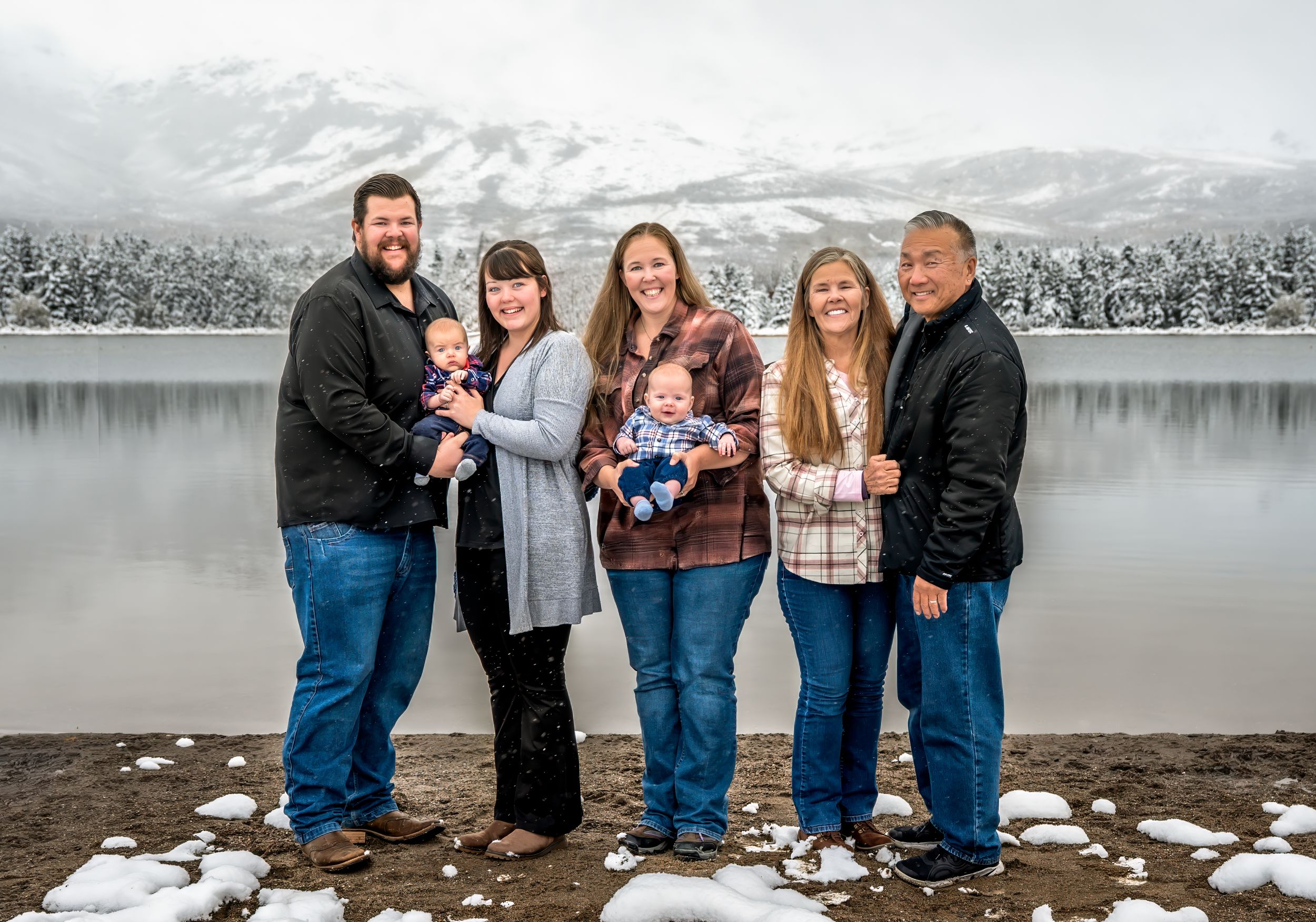 Family group poses together in winter scene by snowy lake with mountains in background.