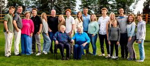 Large group of people wearing casual attire pose together outdoors for a panoramic photo in a grassy area.