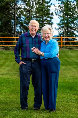 Two people in coordinating blue outfits share joyful laughter together on a grassy lawn on a sunny day.