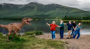 People enjoying outdoor activities near a scenic mountain lake with green hills and cloudy skies in the background.