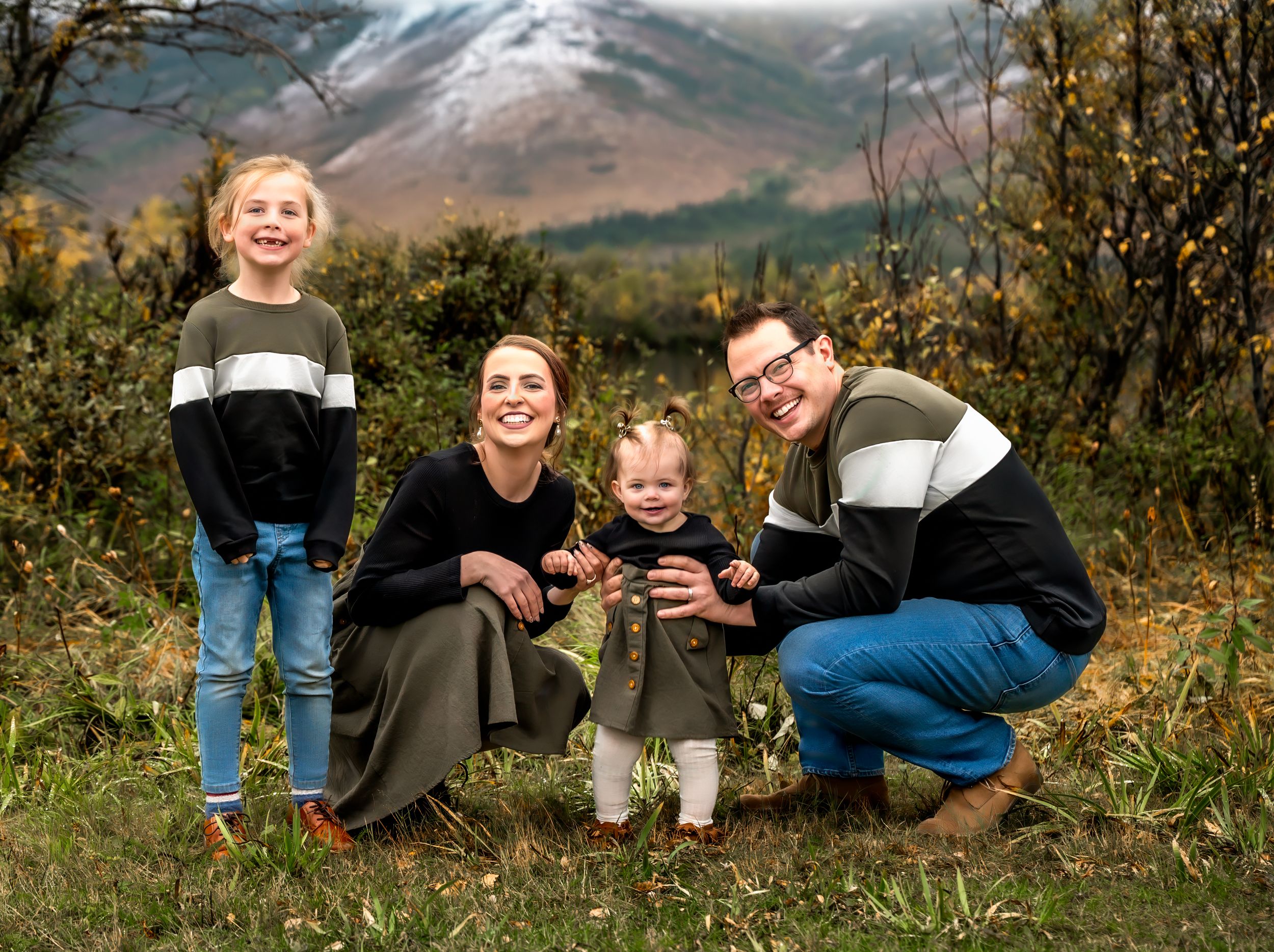 A family poses together outdoors in autumn with snow-capped mountains in the background.