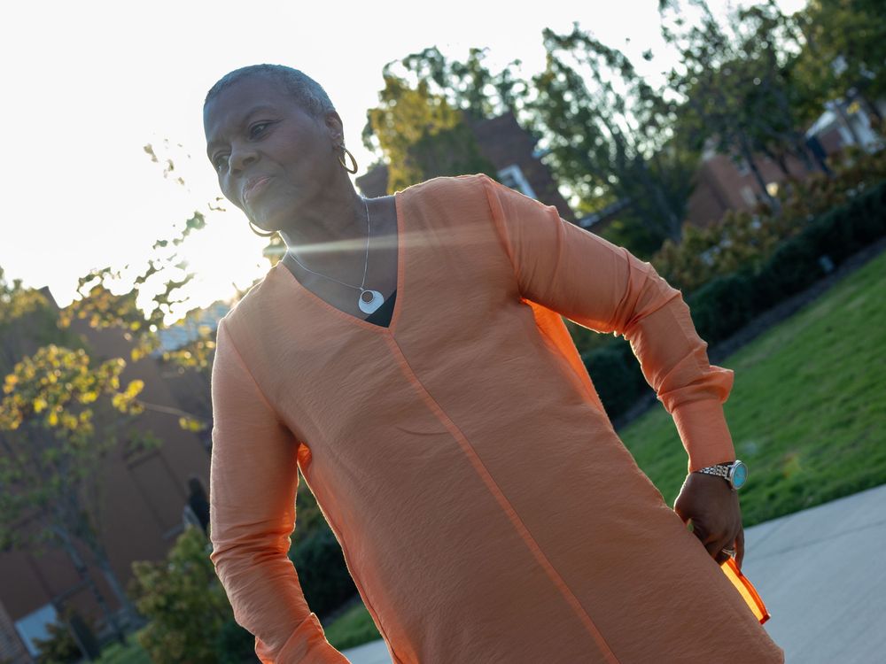 Person wearing a peach-colored sweatshirt stands outdoors in sunlight during golden hour.
