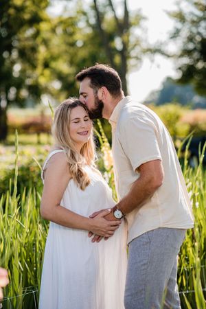 Romantic maternity photo of couple embracing in sunlit field with tall grass.