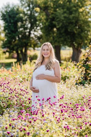 A maternity photo in a wildflower field with pink and purple blooms on a sunny day.