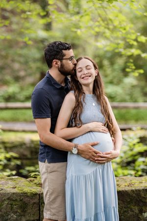 A couple embraces in a lush garden setting with soft natural lighting and greenery in the background.