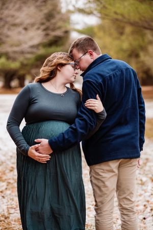 Tender moment between expectant couple embracing outdoors during autumn maternity photoshoot.