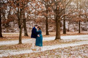 Couple shares intimate moment in winter landscape with fallen leaves and snow-dusted trees.