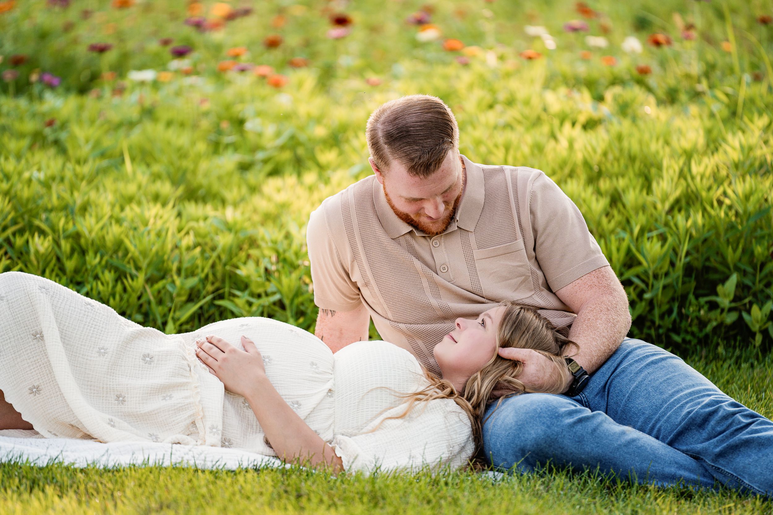 A couple in casual attire relaxes together on green grass during a sunny spring day in the park.