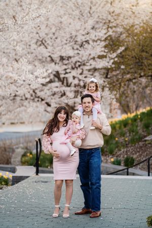 Family portrait in front of cherry blossoms with parents in coordinating outfits.