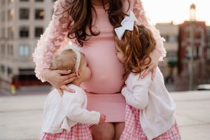 Maternity moment captured with two small children in pink and white dresses.