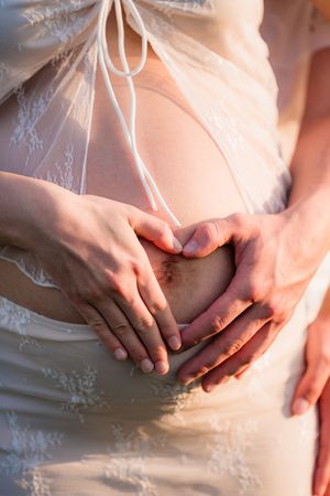 Hands form a heart shape on a white lace wedding dress in soft romantic lighting.