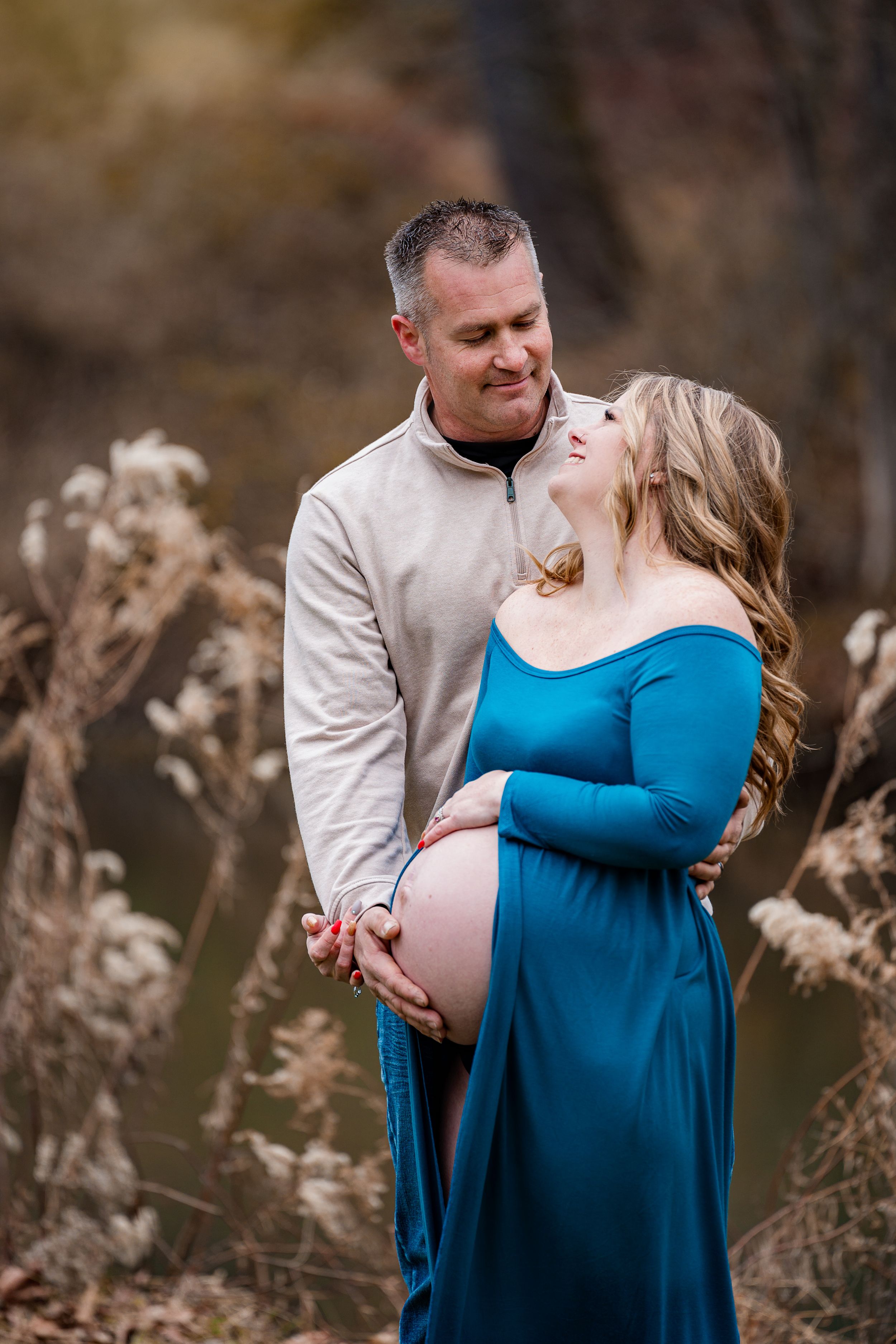 A tender maternity moment captured outdoors with a blue dress and casual attire.