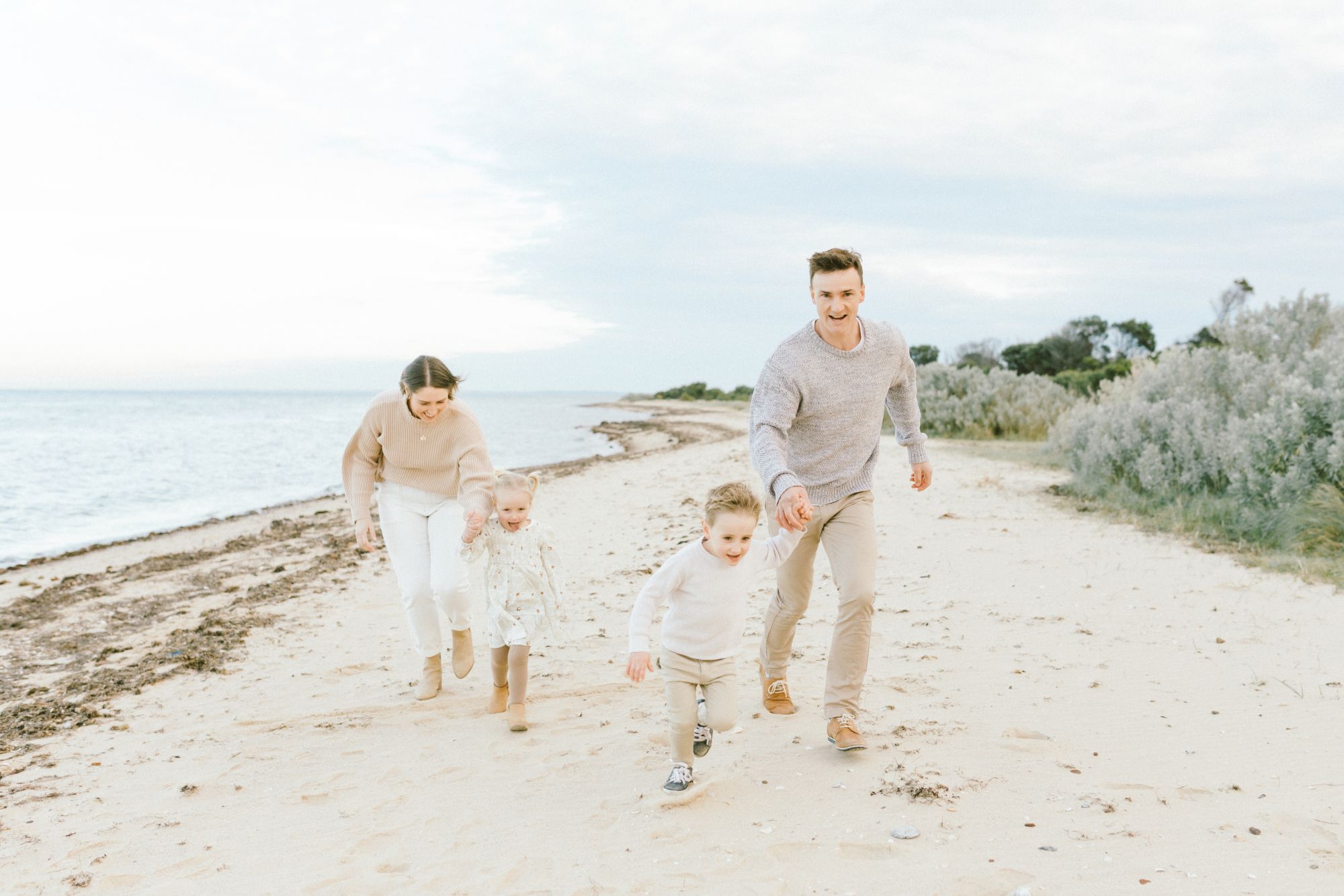 Family walking along sandy beach at sunset with feet in shallow ocean water.