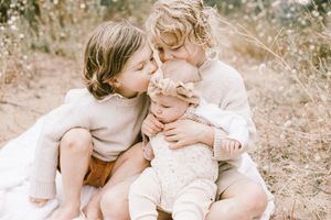 A tender family moment captured in soft, warm tones as they embrace on a sunlit grassy field.