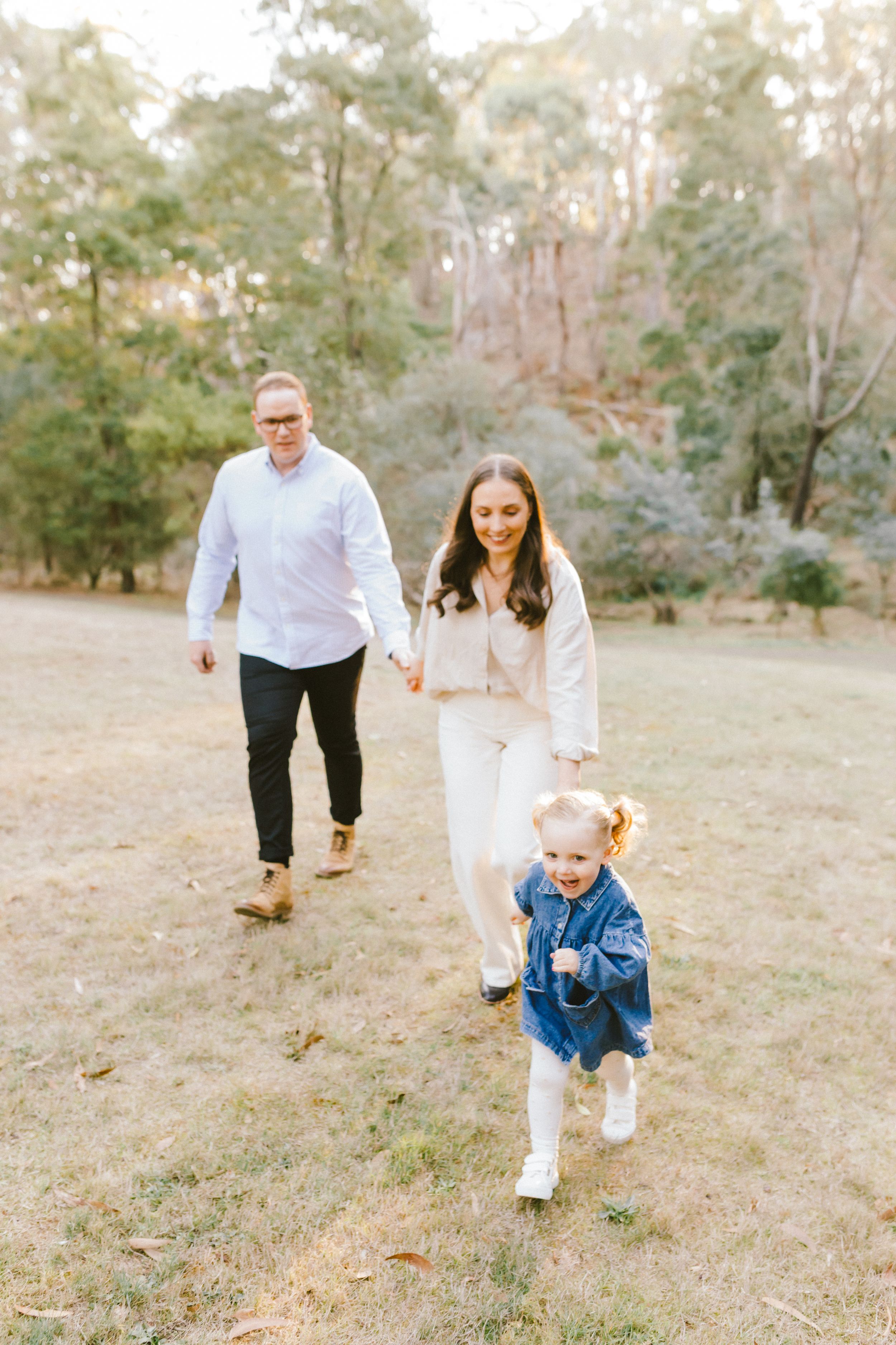 A family plays together and runs through a grassy field on a sunny autumn day.