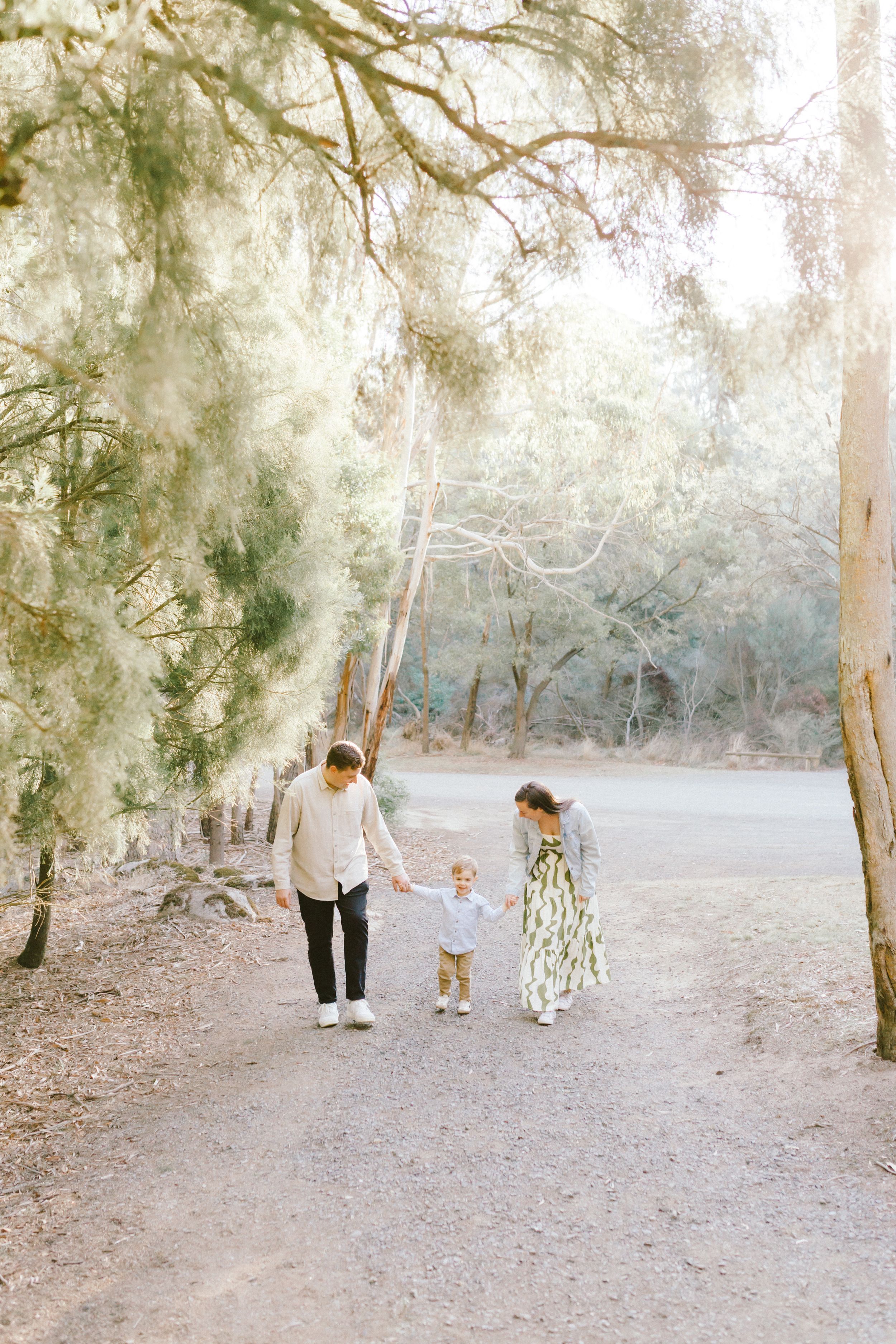 A family walks together on a sunlit dirt path through eucalyptus trees in a dreamy outdoor setting.