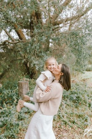 Two people share a tender embrace outdoors surrounded by lush greenery and trees on a bright sunny day.