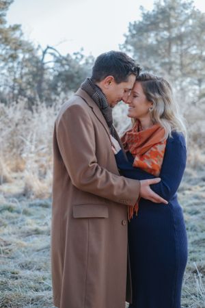 Familienfotografie: Paar steht eng beieinander in winterlicher Natur, die schwangere Frau wird vom Partner gehalten, in Pfaffenhofen (Ilm).